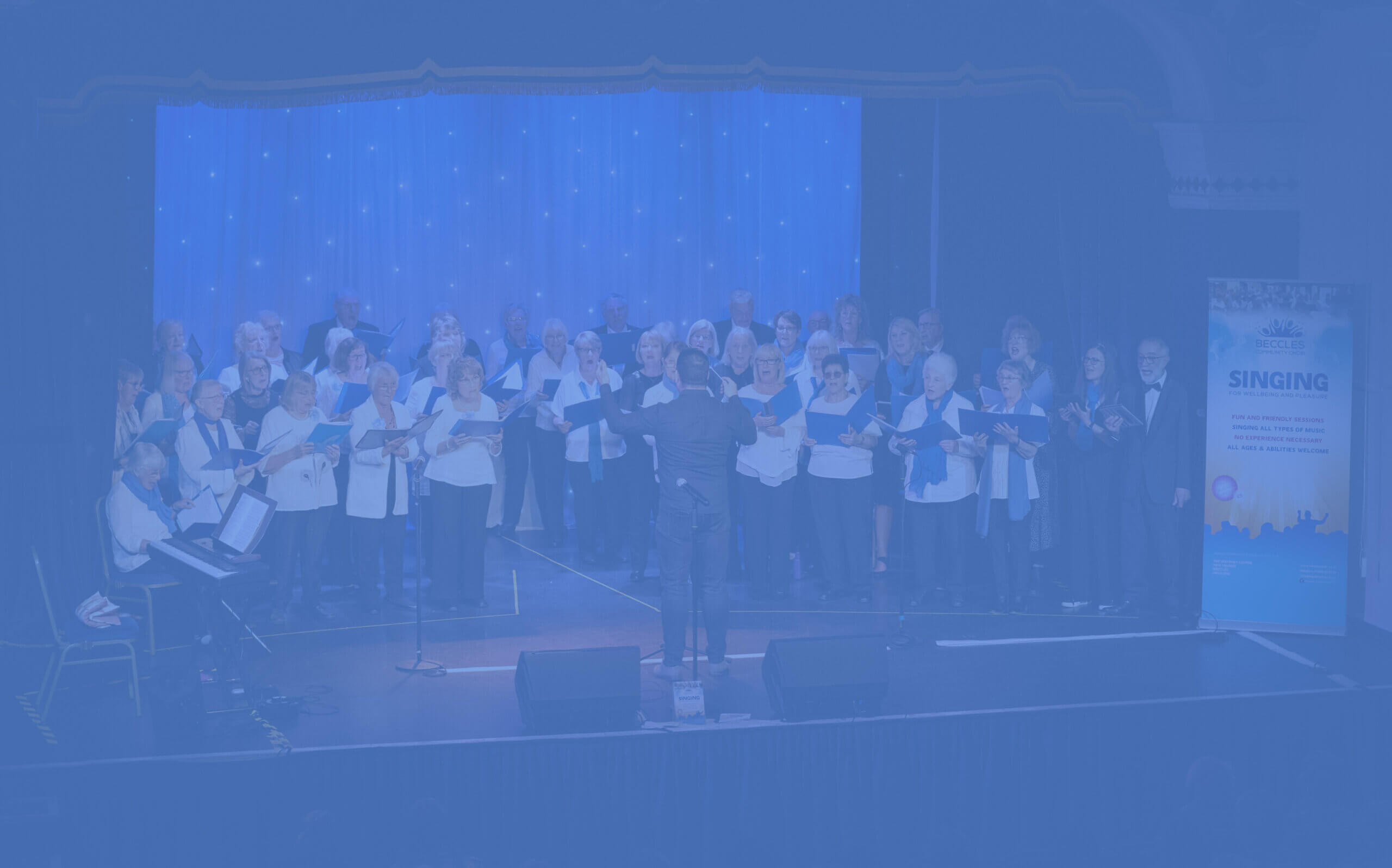 People on a stage holding blue folders and singing with conductor in the middle leading them